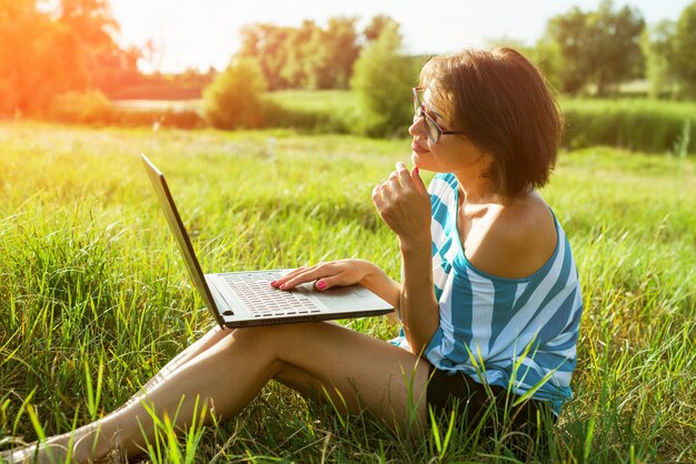 Schöne erwachsene Frau, die auf Laptop schreibt