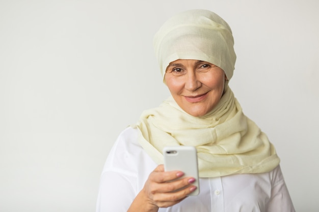 schöne erwachsene Frau im Alter in einem muslimischen Kopftuch mit einem Handy