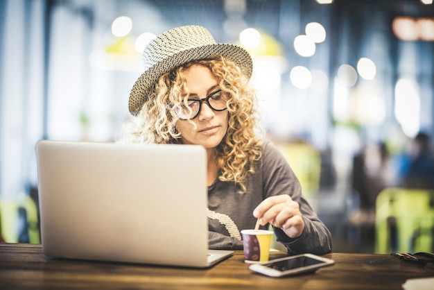 Schöne erwachsene junge Frau bei der Arbeit mit Laptop-Kocomputer in einem Café-Restaurant am Flughafen, die auf ihren Flug wartet - digitales Nomaden- und modernes Menschen-Online-Job-Technologie-Konzept