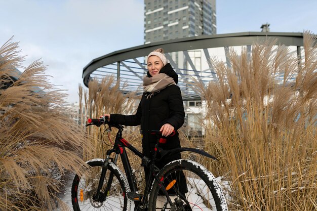 Schöne europäische Frau mit Kopfband, die einen schwarzen langen Mantel trägt und Fahrrad fährt