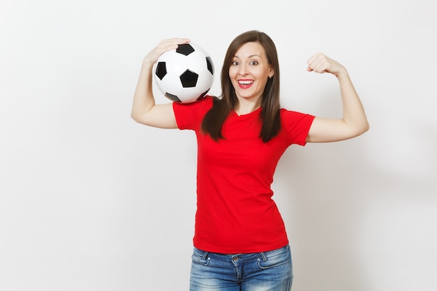 Schöne europäische junge starke schlanke Frau, Fußballfan oder Spieler in roter Uniform, die klassischen Fußball isoliert auf weißem Hintergrund hält. Sport, Fußball spielen, Gesundheit, gesundes Lebensstilkonzept.