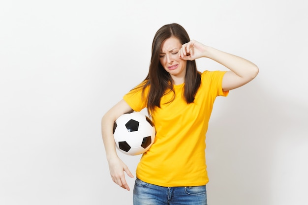 Schöne europäische junge verärgerte weinende Frau, Fußballfan oder Spieler in der gelben Uniform, die Fußball lokalisiert auf weißem Hintergrund hält. Sport, Fußball spielen, Gesundheit, gesundes Lebensstilkonzept.