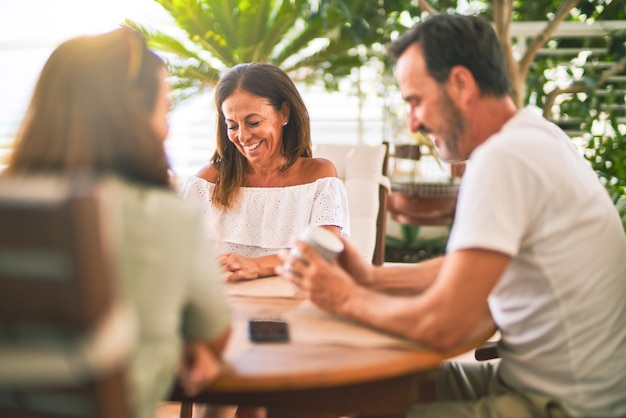 Schöne Familie, die auf der Terrasse sitzt und eine Tasse Kaffee trinkt, spricht und lächelt