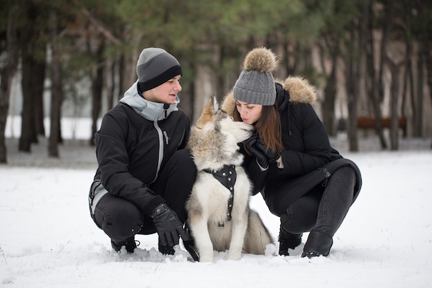 Schöne Familie, ein Mann und ein Mädchen im Winterwald mit Hund. Spielen Sie mit dem Hund Siberian Husky.