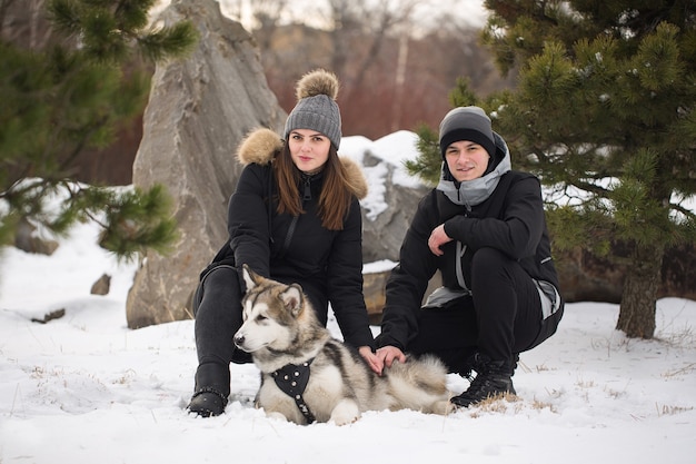 Schöne Familie, ein Mann und ein Mädchen im Winterwald mit Hund. Spielen Sie mit dem Hund Siberian Husky.