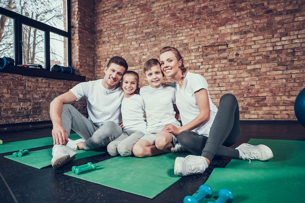 Schöne Familie in den weißen T-Shirts, die in der großen Turnhalle sitzen.