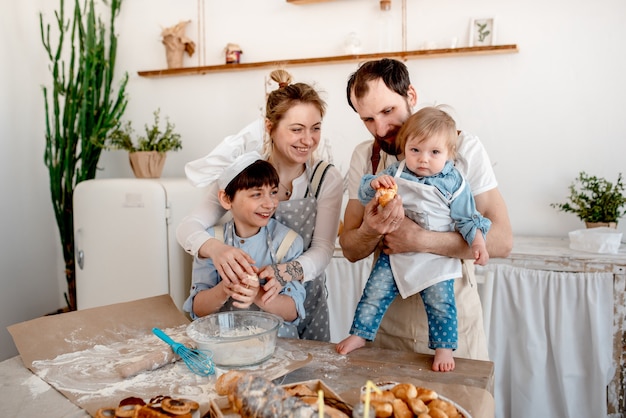 Schöne Familie von Mama, Papa und zwei Kindern bereitet Teig und Umarmungen in der Küche