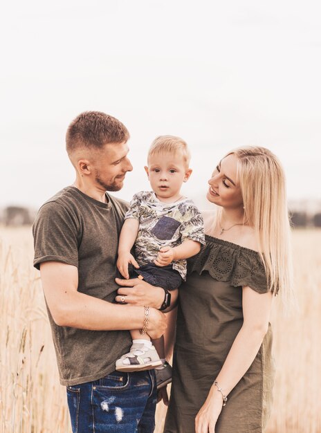 Schöne Familieneltern und ein junger Sohn auf einem Weizengebiet. Mama, Papa und Baby zusammen. Glückliche Familie, Eltern umarmen ihren kleinen Sohn