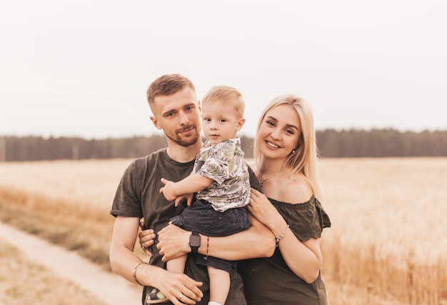 Schöne Familieneltern und ein junger Sohn auf einem Weizengebiet. Mama, Papa und Baby zusammen. Glückliche Familie, Eltern umarmen ihren kleinen Sohn