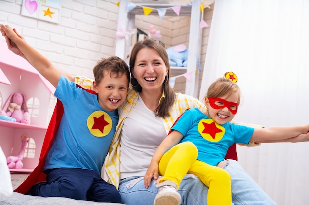 Schöne Familienmutter und -tochter mit dem Sohn kleideten in den Kostümen von Superhelden an