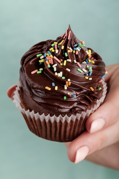 Schöne feminine Hand hält lecker appetitlich Schokolade Cupcake. Blauer Hintergrund. Nahansicht.