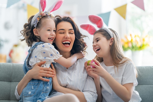 Schöne Ferien! Mutter und ihre Töchter mit bemalten Eiern. Familie feiert Ostern. Nette kleine Kindermädchen tragen Hasenohren.