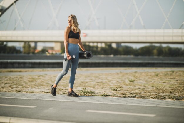 Schöne fitte Frau, die in der Nähe der Flussbrücke in der Stadt spazieren geht und sich auf das Training im Freien vorbereitet.