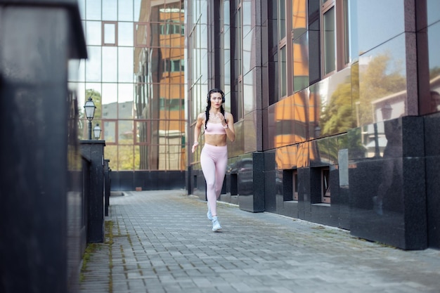 Schöne, fitte Frau-Läuferin mit Schwanz, die gegen den Hintergrund eines Stadtgebäudes joggt