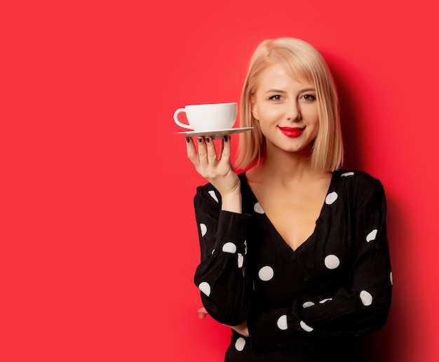 Schöne französische Frau hält Tasse Kaffee auf roter Wand