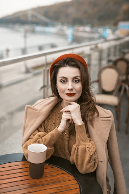 Schöne französische Frau trinken Kaffee mit Kaffeetasse, die an Restaurantterrasse mit Kaffeetasse sitzt