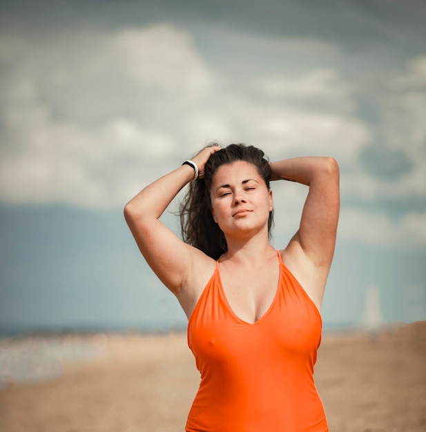 Schöne Frau 40 Jahre alt plus Größe, am Strand in einem orangefarbenen Badeanzug, Thema Körperpositivität