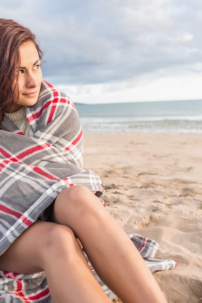 Schöne Frau bedeckt mit Decke am Strand