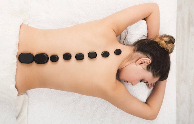 Foto schöne frau bei der massage mit heißen steinen im spa-salon. schönheitsbehandlungstherapie, wellness- und entspannungskonzept, draufsicht