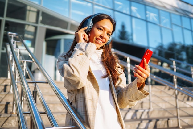 Schöne Frau benutzt ein Mobiltelefon in der Stadt, während sie Musik durch Kopfhörer hört Musik Emotionen