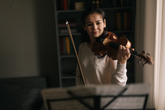 Schöne Frau betrachtet die Partitur, während sie Geige spielt. Mädchen übt das Spielen von Musikinstrumenten zu Hause.