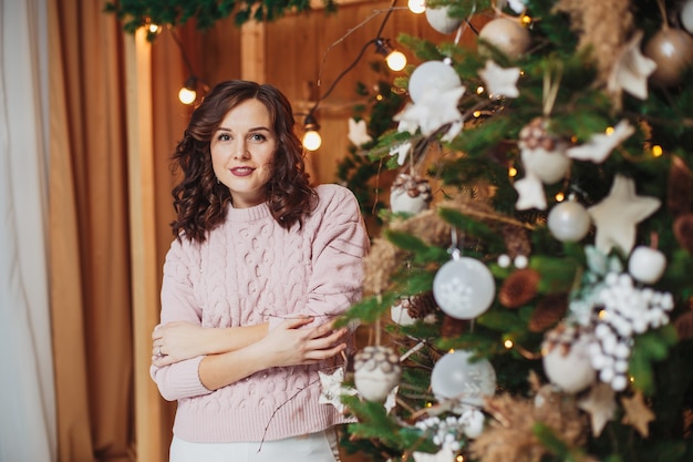 Schöne Frau Brünette im rosa Pullover, posierend in der Nähe von Weihnachtsbaum