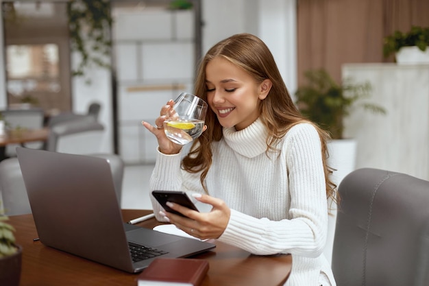 Schöne Frau, die am Tisch im Büro sitzt und Wasser trinkt