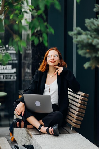 Schöne Frau, die an einem Laptop im Café im Freien arbeitet