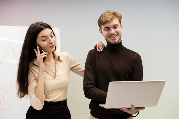 Schöne Frau, die auf dem Smartphone spricht, lächelnder Mann, der am Laptop arbeitet, während er in einem modernen Büro steht