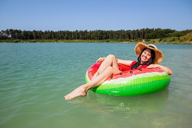 Schöne Frau, die auf einem aufblasbaren Ring im sonnigen Sommertag des blauen Seewassers schwimmt