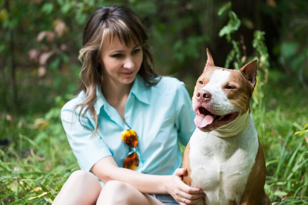 Schöne Frau, die auf Gras mit Hund Pitbull sitzt