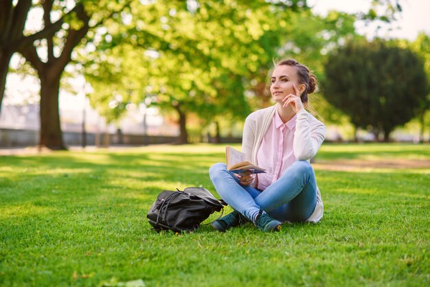 Schöne frau, die auf gras sitzt und buch im park im sommer liest