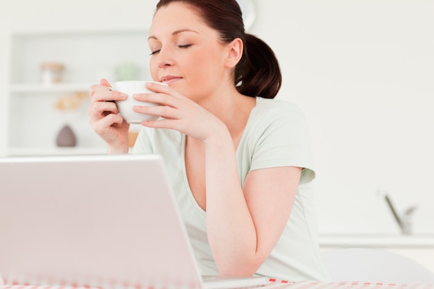 Schöne Frau, die auf ihrem Laptop beim Trinken einer Tasse Tee sich entspannt