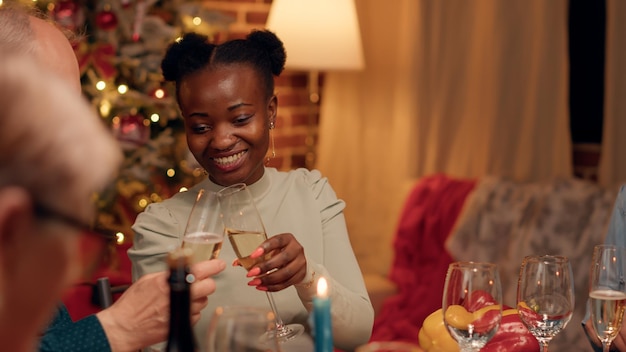 Schöne Frau, die beim Weihnachtsessen mit einer älteren Person spricht, während sie traditionelle hausgemachte Speisen isst. Festliche, vielfältige Familienmitglieder, die das Winterfest mit Champagner feiern.