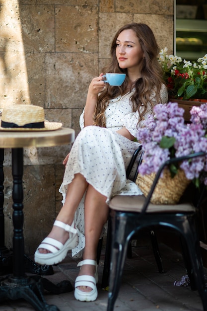 Schöne Frau, die den Morgenkaffee nahe lila Blüte genießt. Nettes Modell und Blumen. Aromatherapie und Frühlingskonzept. Mädchen trinken Kaffee im Café.