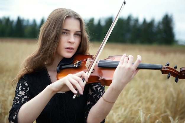 Schöne Frau, die die Geige im Weizenfeld spielt