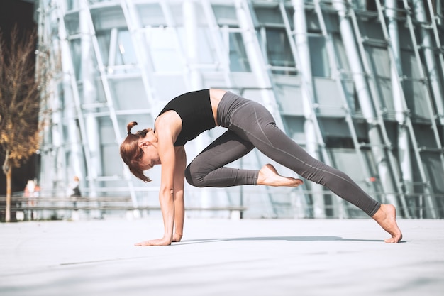 Schöne Frau, die draußen in der Stadt Stretching-Yoga-Übungen macht