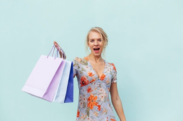 Schöne Frau, die ein Kleid mit Einkaufstaschen auf blauem Hintergrund trägt. Konzept des Einkaufens von Einkäufen und Verkäufen