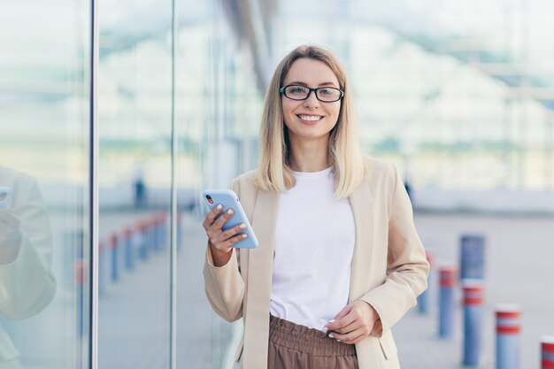 Schöne Frau, die ein Telefon in den Händen hält und in die Kamera schaut