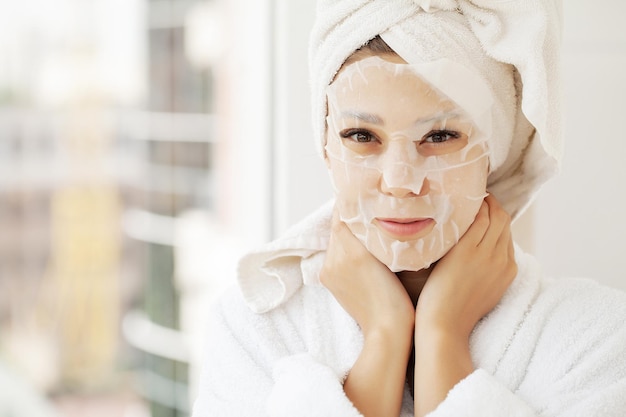 Schöne Frau, die eine Blattmaske aus Papier auf ihrem weißen Gesicht anwendet