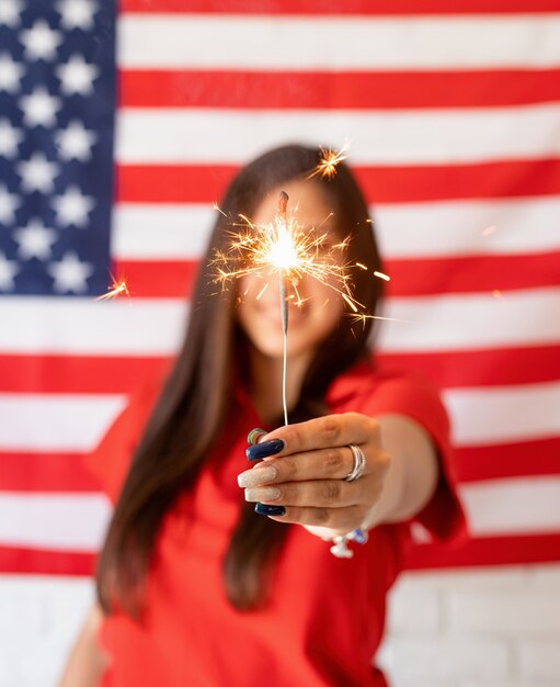 Schöne Frau, die eine Wunderkerze auf dem US-Flaggenhintergrund hält