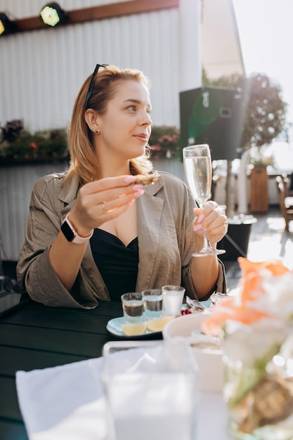 Schöne Frau, die frische Austern isst und gekühlten Prosecco-Wein bei Sommersonnenuntergang im Restaurant mit Meeresfrüchten trinkt