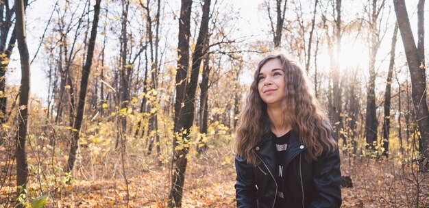 Schöne Frau, die im Herbstwald steht Mädchen in schwarzer Lederjacke, die im Wald spazieren geht