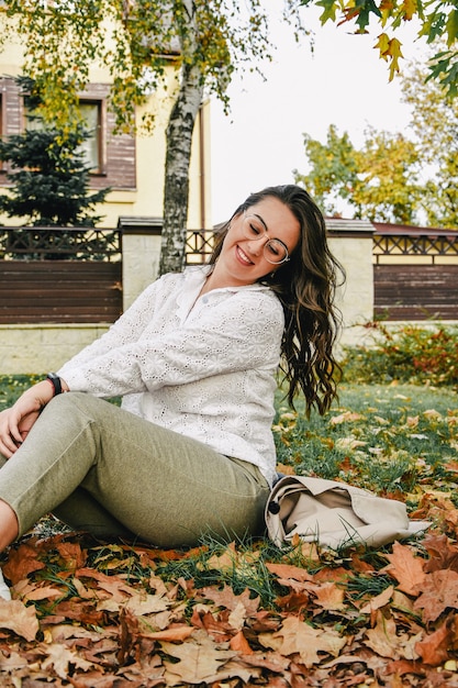 Schöne Frau, die im Park sitzt. Herbst Natur. Lebensstil. Porträt eines schönen weiblichen Modells im Herbst kleidet sensiblen Blick im Freien. Pastellfarben. Herbstkonzept