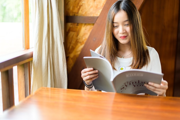 Schöne Frau, die in einem Café sitzt, das eine Zeitschrift liest