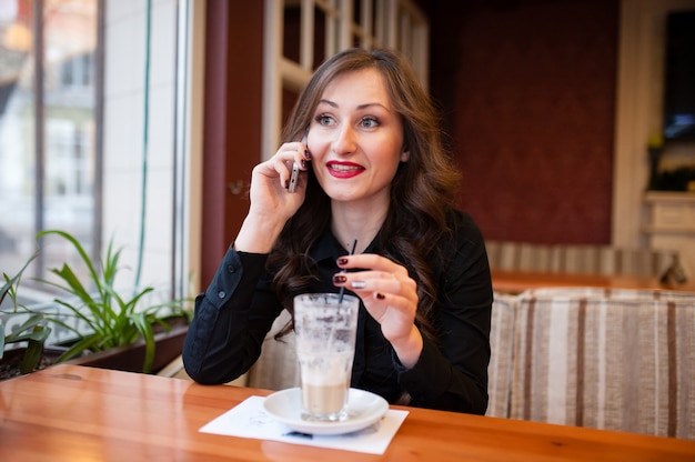 Schöne Frau, die Kaffee trinkt und am Telefon spricht