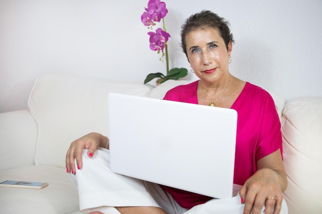 Schöne Frau, die Krebs in einer fuchsiafarbenen Bluse mit Laptop überwunden hat, während sie lächelt.
