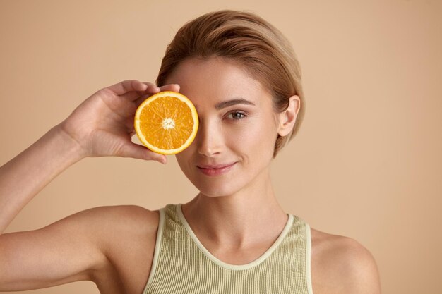 Schöne Frau, die mit orange Frucht lächelt Frau empfohlenes Vitamin für Haut