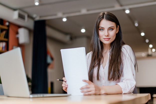 Schöne Frau, die mit Papieren und Laptop im Büro arbeitet