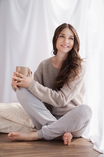 Schöne Frau, die morgens Kaffee trinkt und am Fenster sitzt